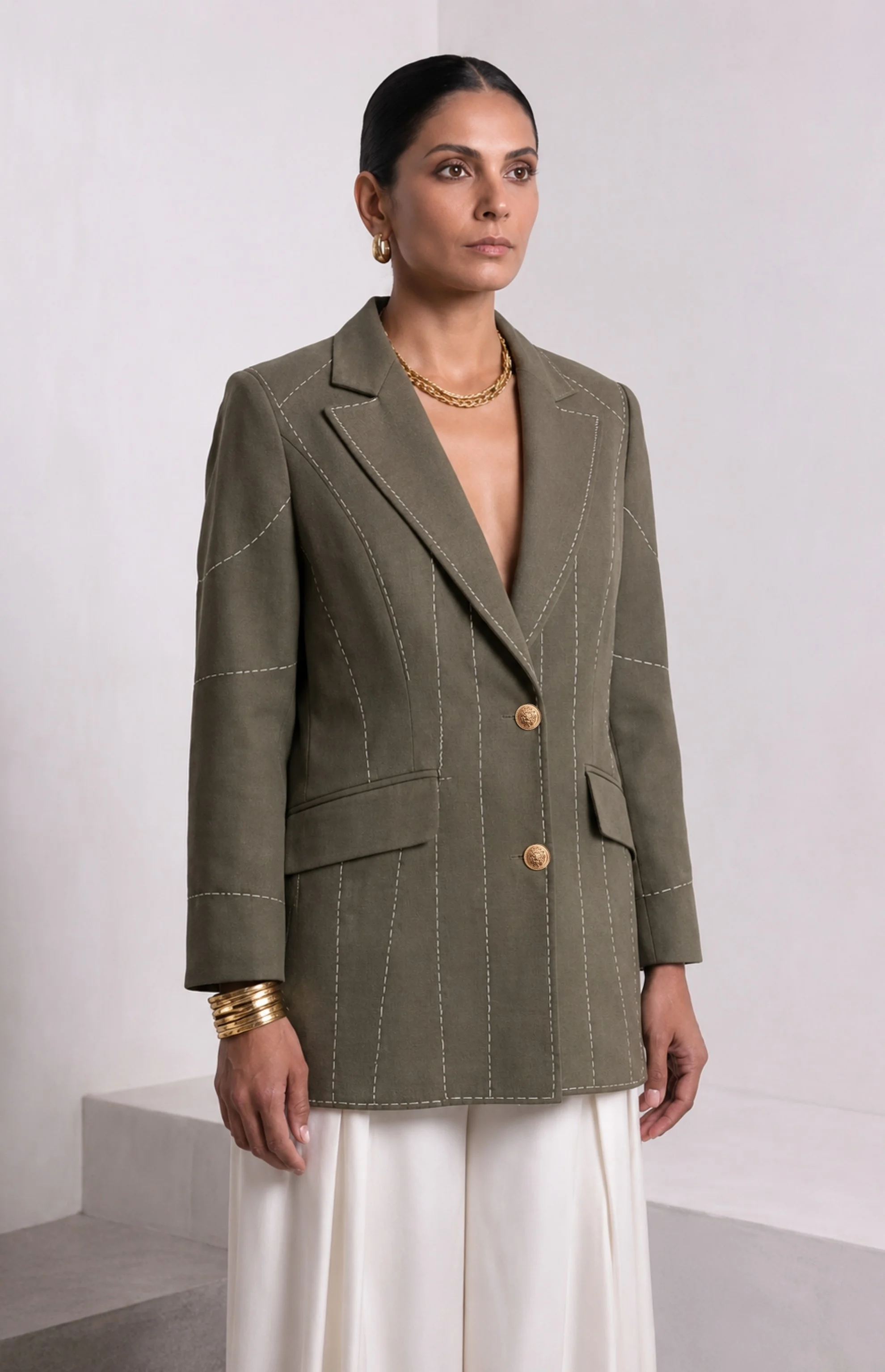 Front view of dark olive green Debrief blazer with contrast white stitching and gold buttons.