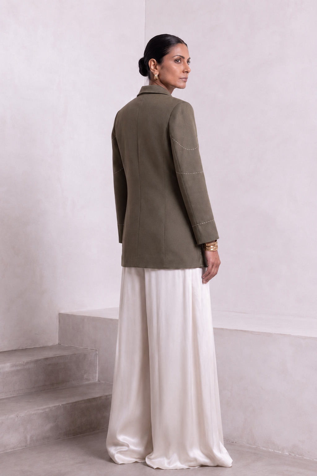 Back view of dark olive green Debrief blazer showing center-back seam and contrast stitch detailing on the sleeves.