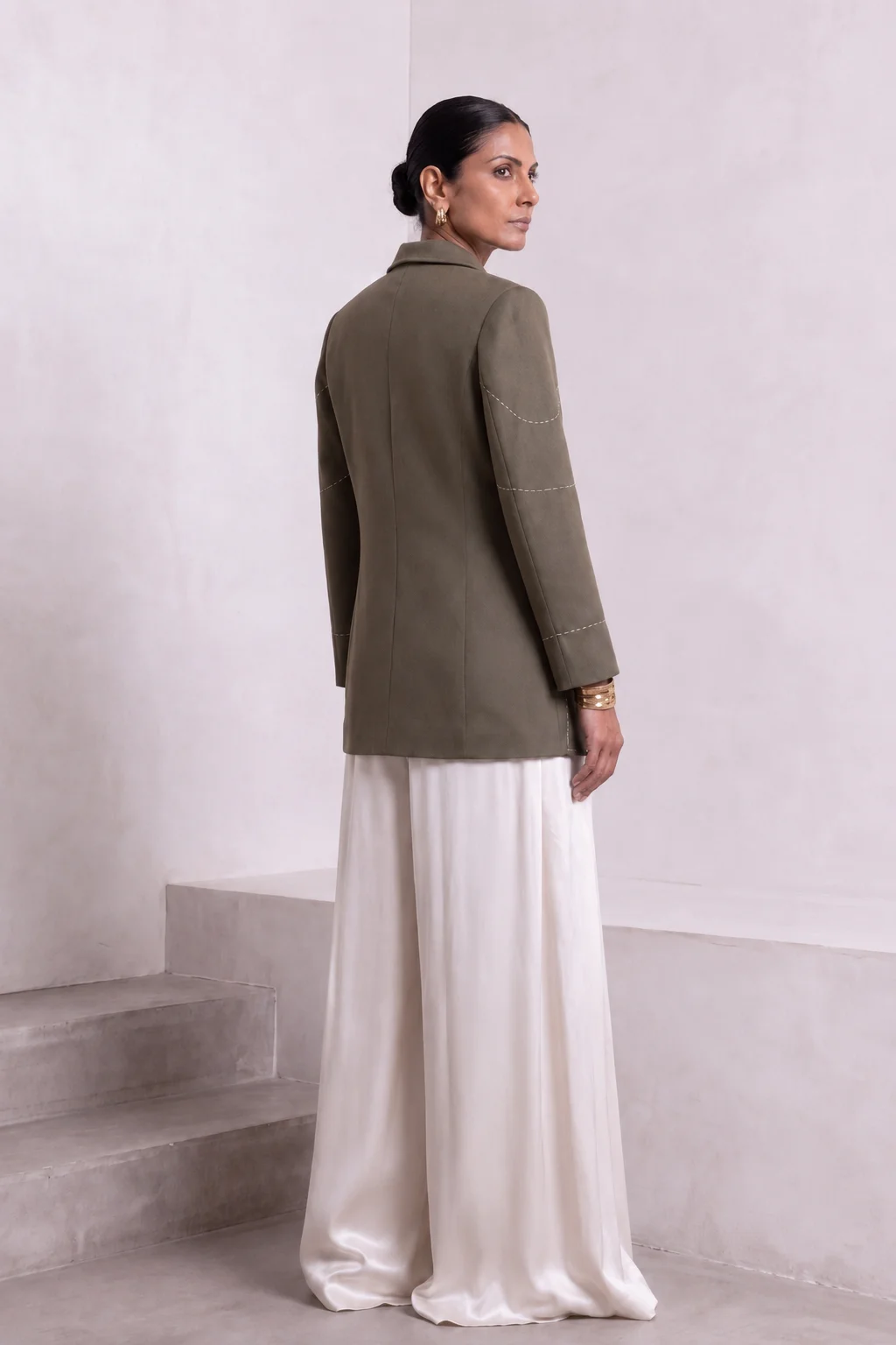 Back view of dark olive green Debrief blazer showing center-back seam and contrast stitch detailing on the sleeves.