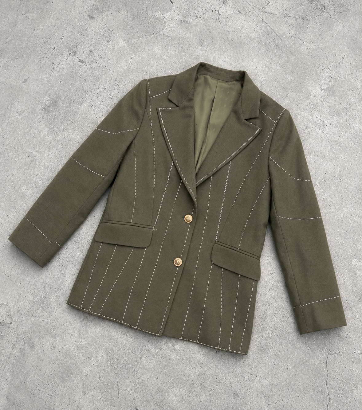 Flat lay of dark olive green Debrief blazer showing lapels, gold buttons and contrast white stitching.