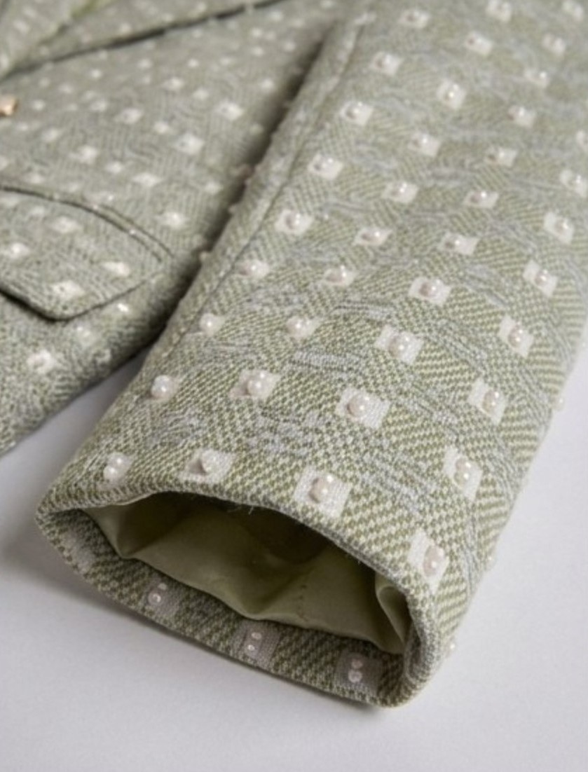 Close-up of light sage green Ping Me blazer sleeve showing embroidered detail and cuff lining.