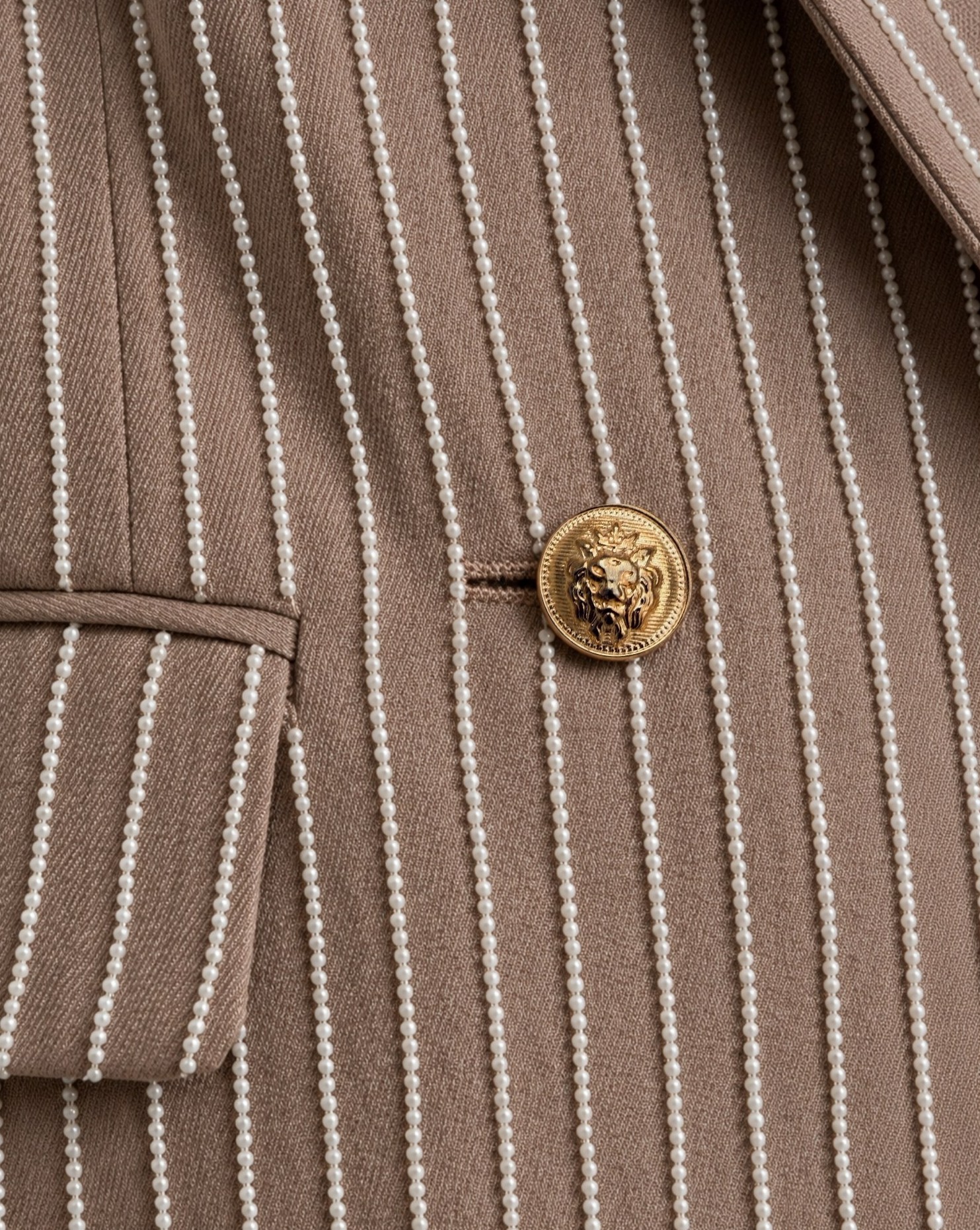 Close-up of taupe EOD blazer showing pearl-beaded stripes, flap pocket and gold lion-head button.