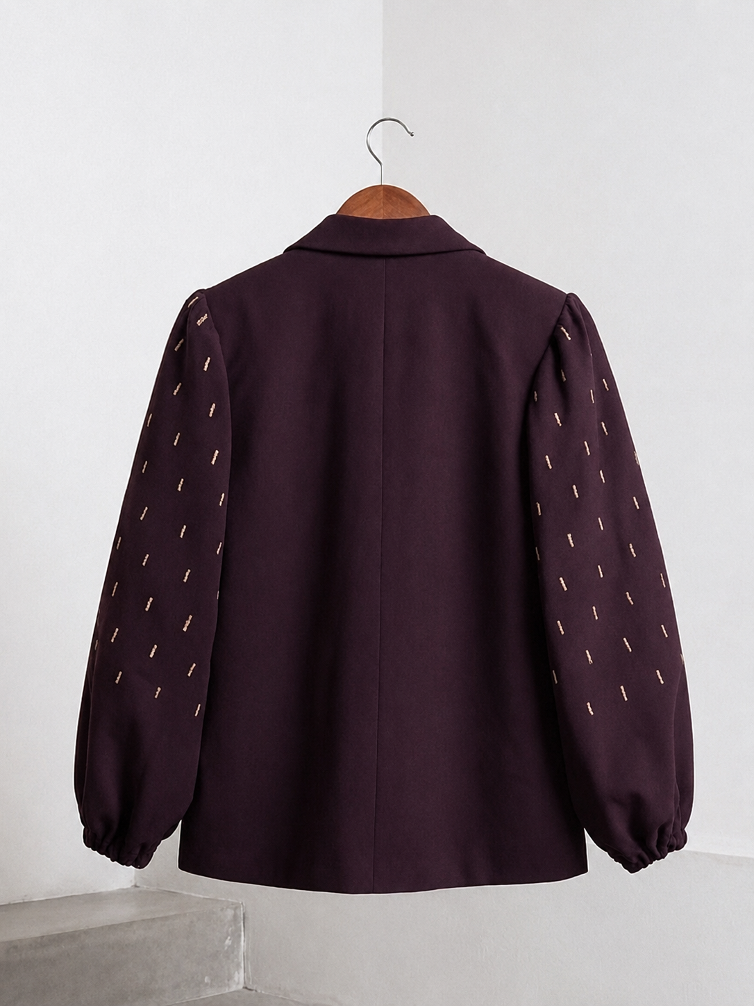 Back view of plum blazer with gold embroidered balloon sleeves on a wooden hanger.