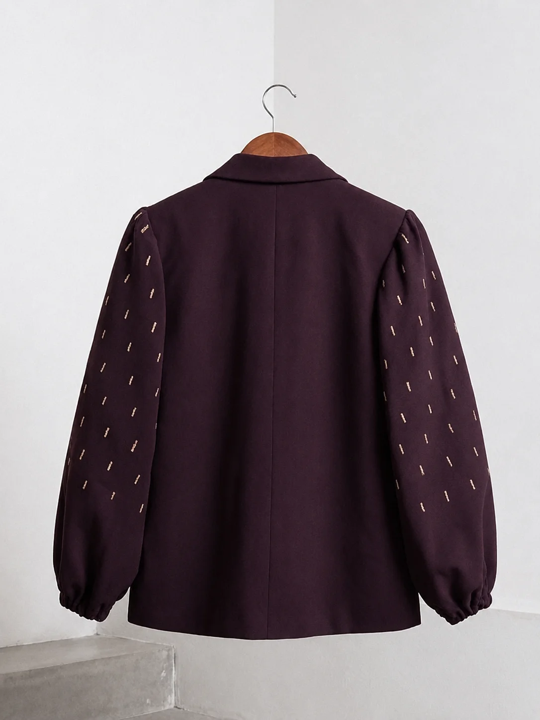 Back view of plum blazer with gold embroidered balloon sleeves on a wooden hanger.