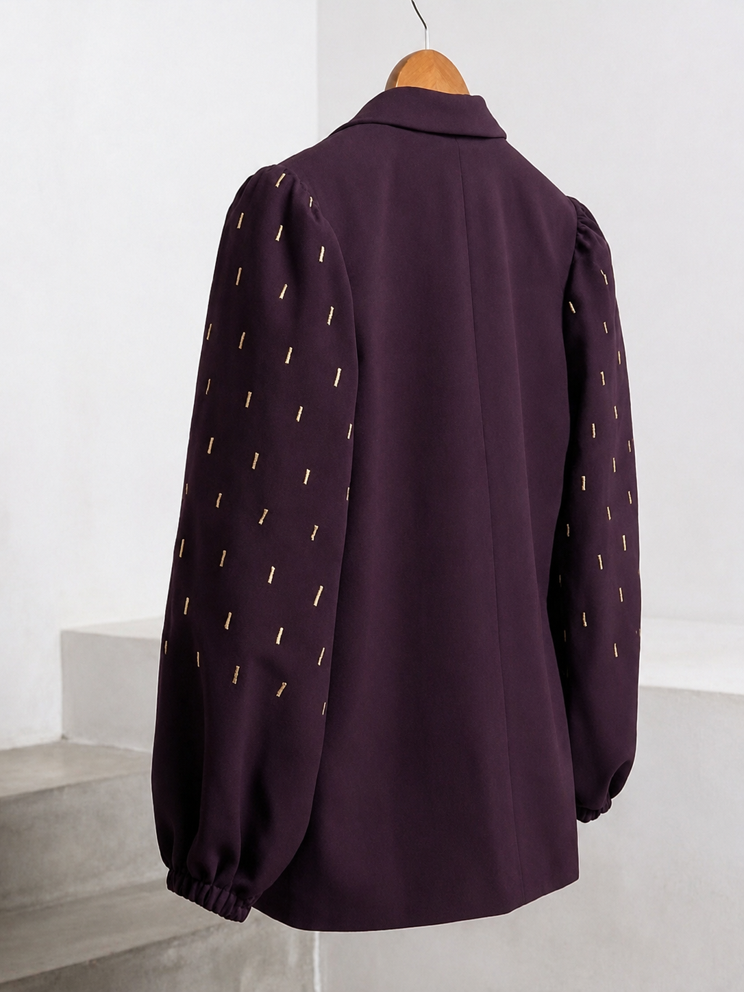 Angled back view of plum blazer with gold embroidered balloon sleeves on a wooden hanger.