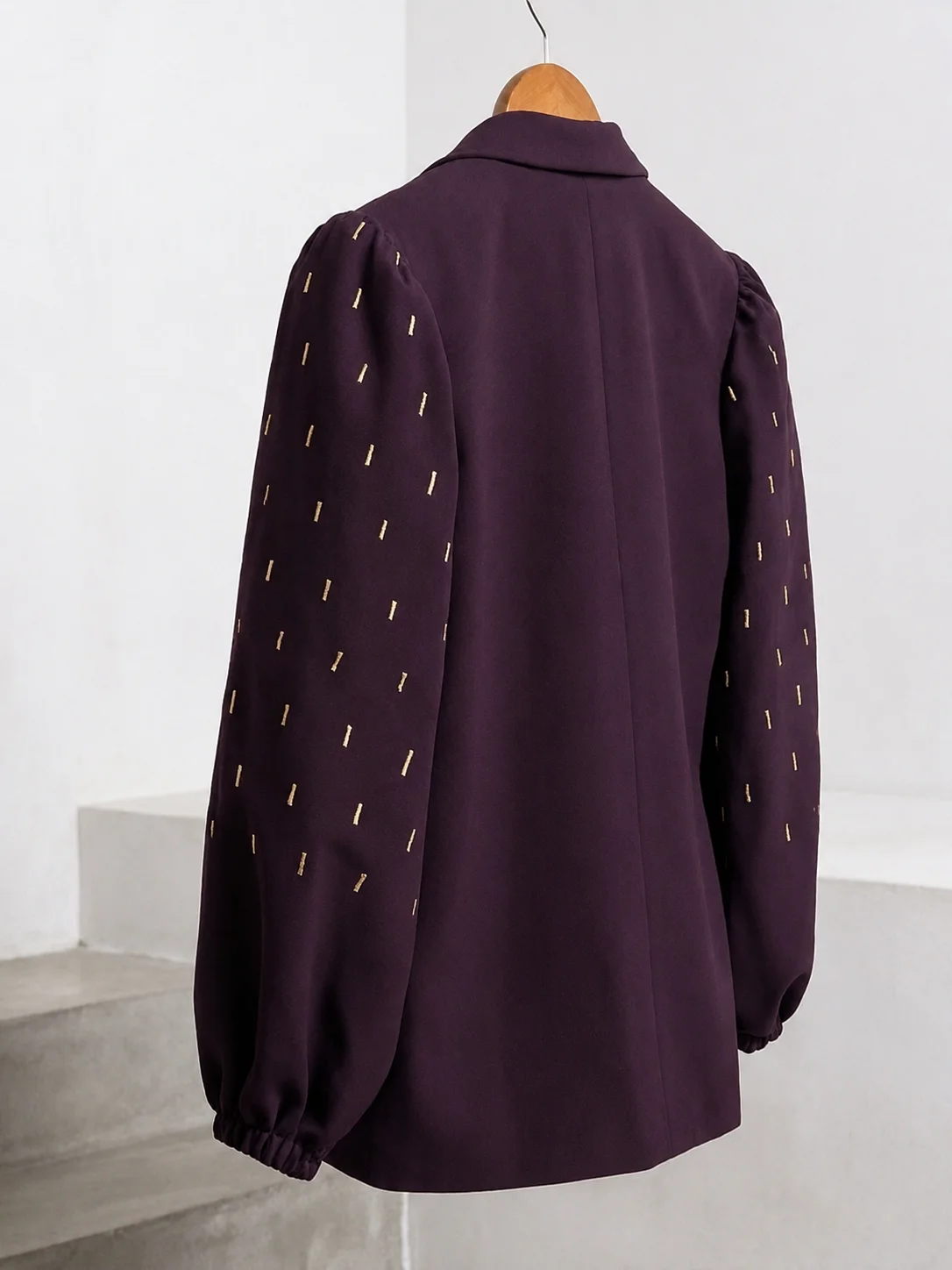 Angled back view of plum blazer with gold embroidered balloon sleeves on a wooden hanger.