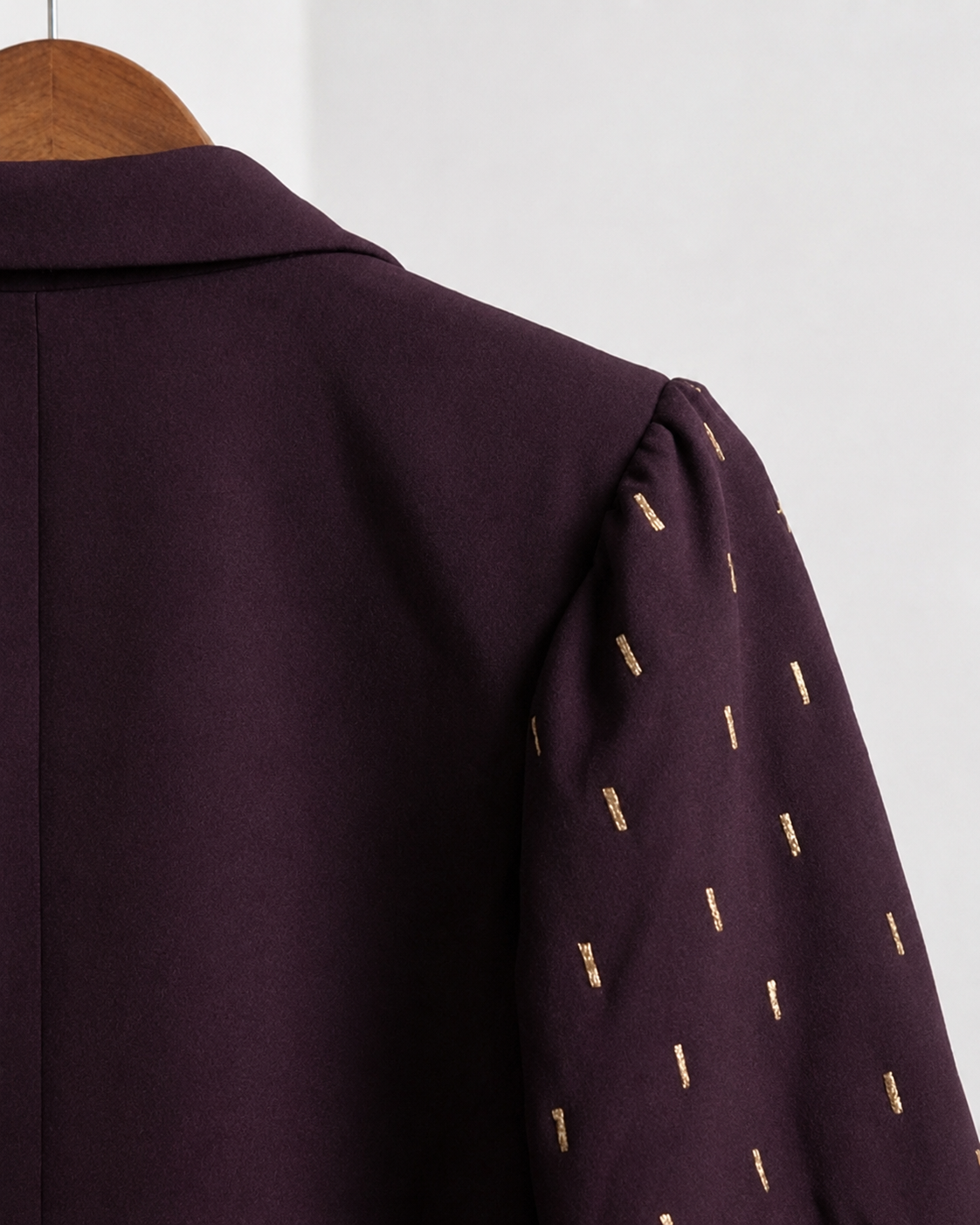 Close-up of plum blazer shoulder with gold embroidered sleeve detail.