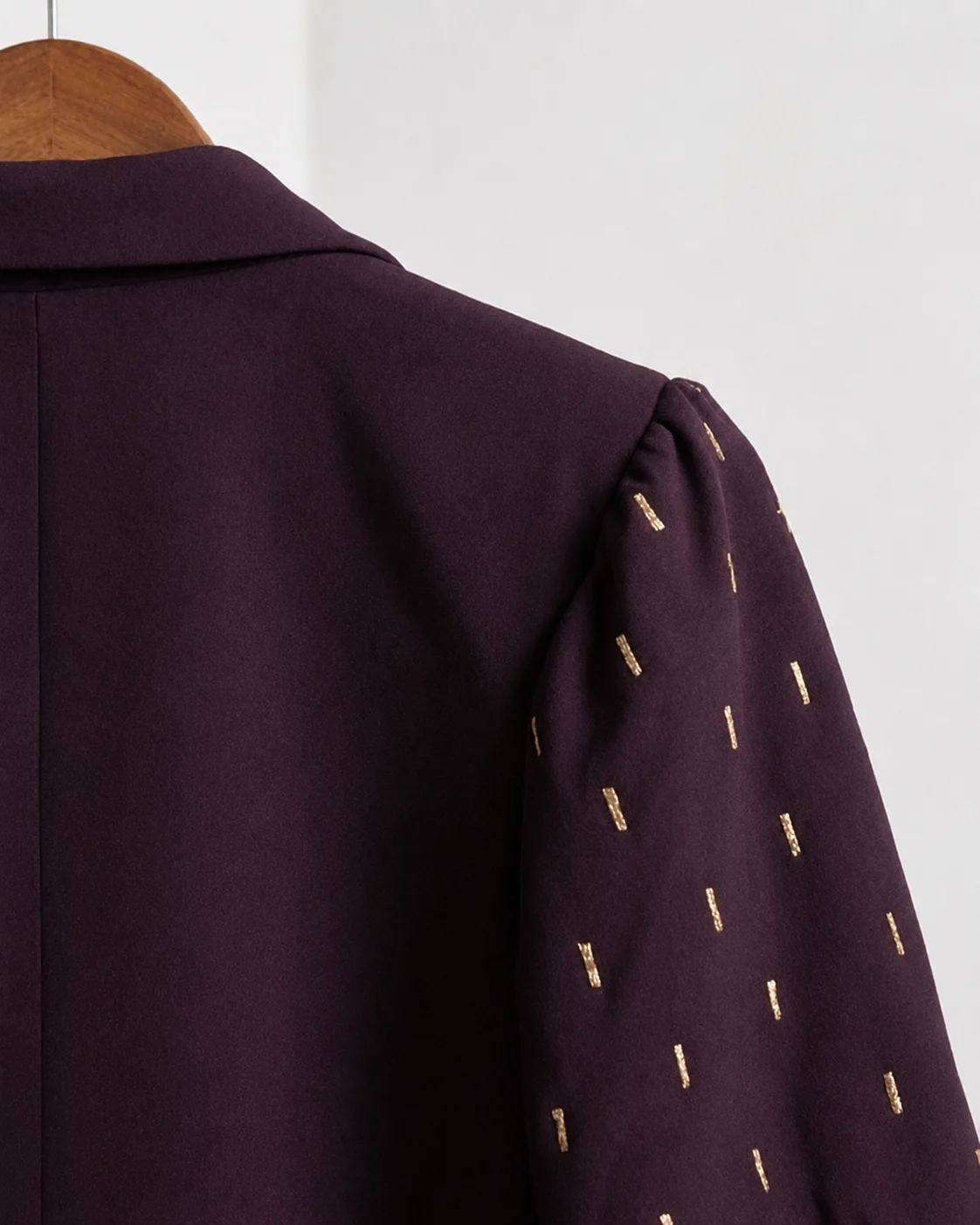 Close-up of plum blazer shoulder with gold embroidered sleeve detail.