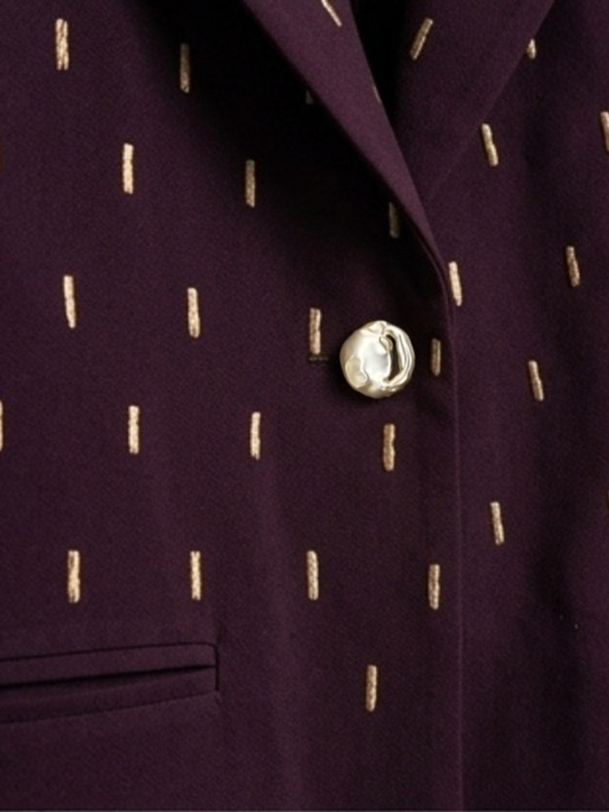 Close-up of plum blazer with gold embroidery and sculptural gold-tone button.