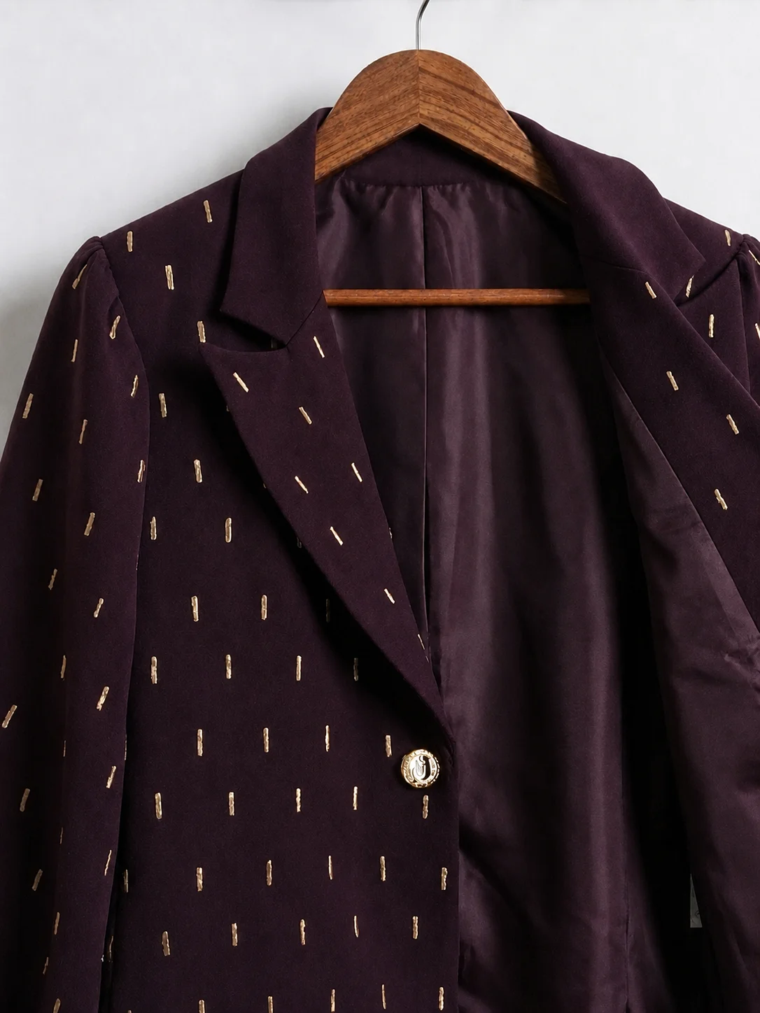Front detail of plum blazer showing gold embroidery, lapel, lining and gold-tone button.