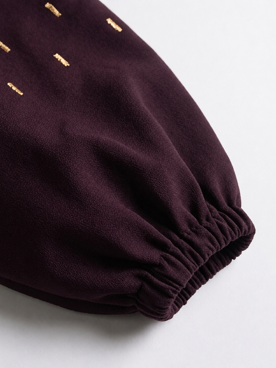 Close-up of plum blazer sleeve showing gold embroidery and gathered elasticated cuff.