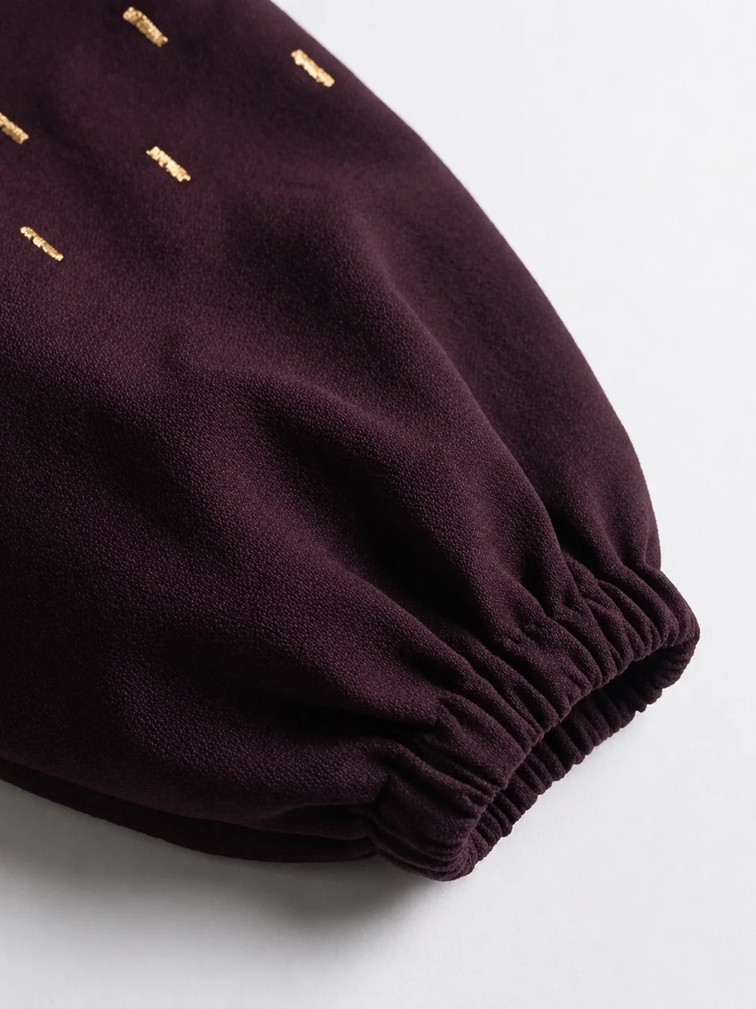 Close-up of plum blazer sleeve showing gold embroidery and gathered elasticated cuff.