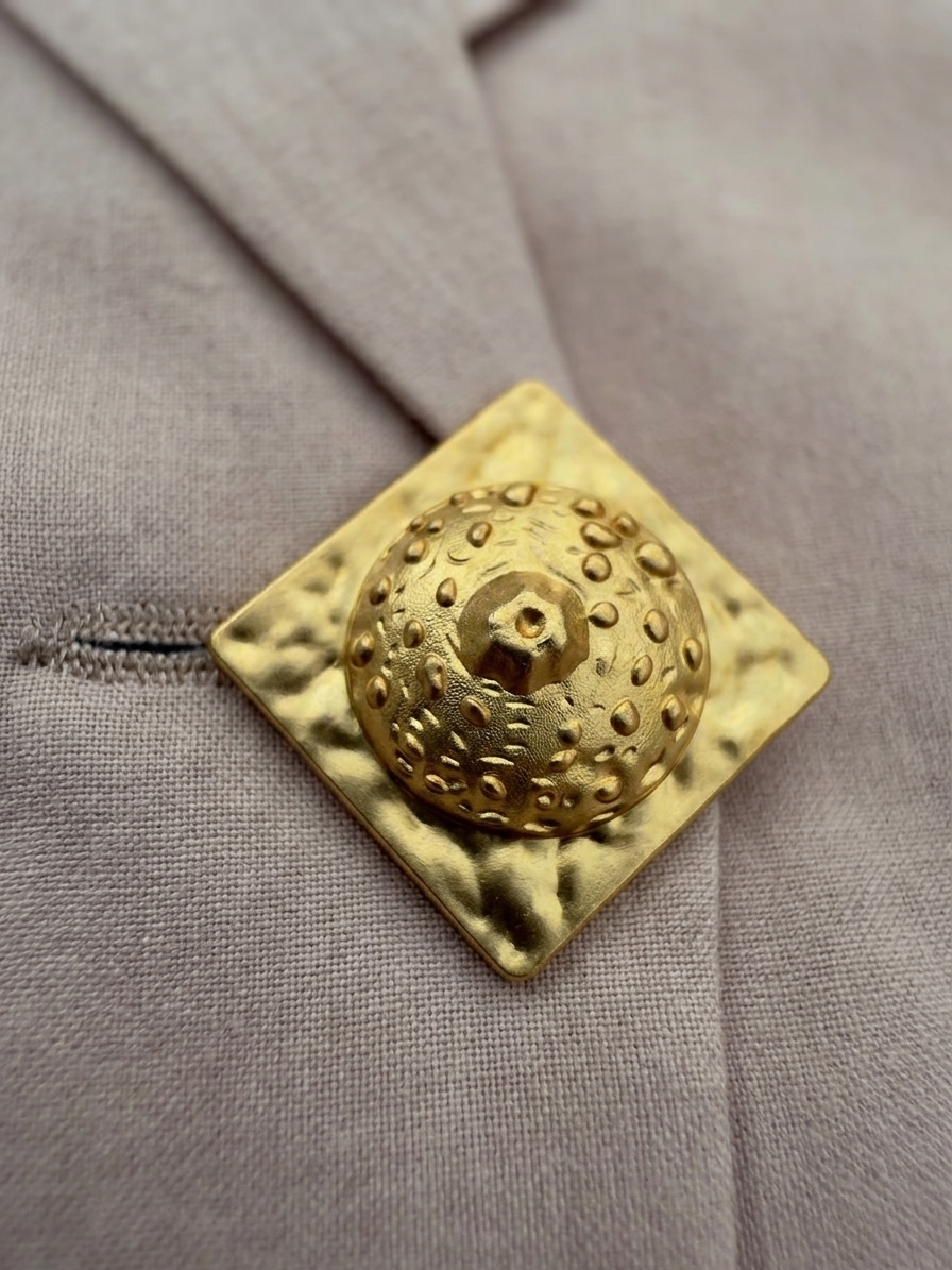 Close-up of statement gold-tone button on beige Disconnect tailored vest.