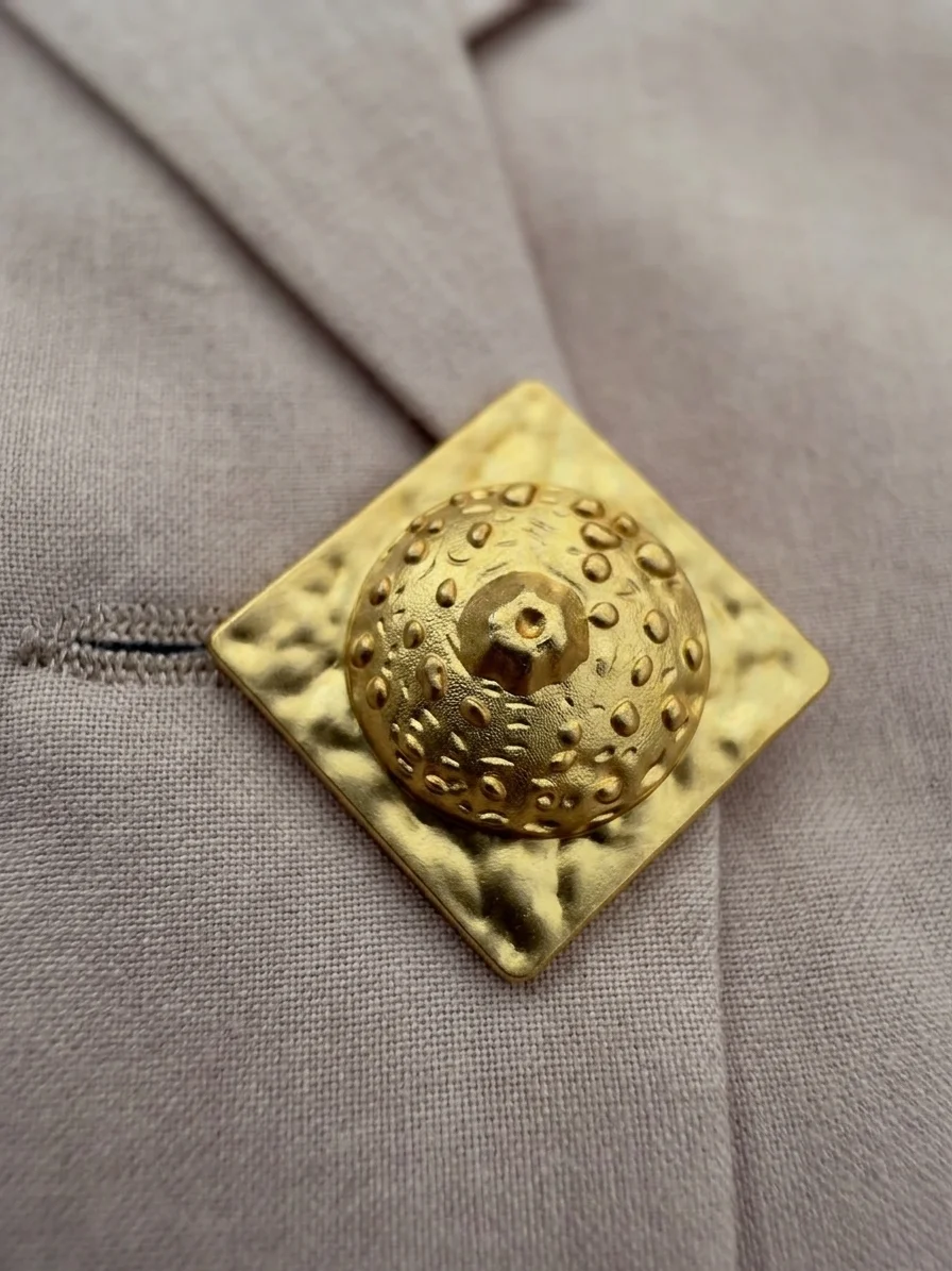 Close-up of statement gold-tone button on beige Disconnect tailored vest.