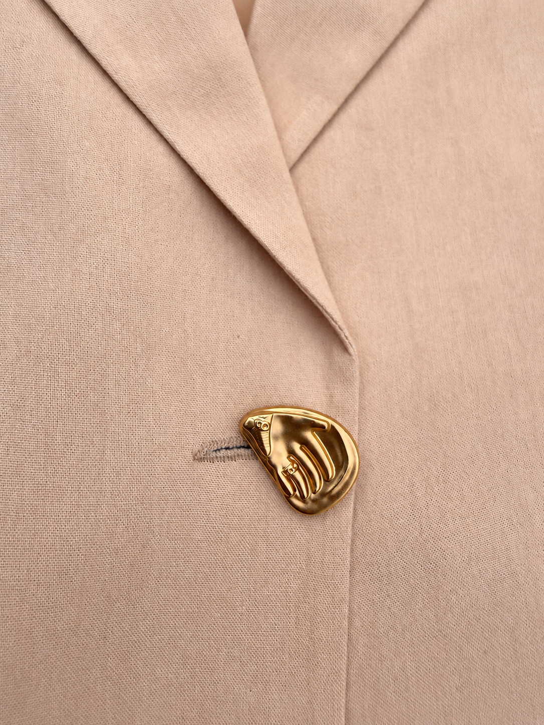 Close-up of sculptural gold-tone button on the beige Brainstorm blazer.