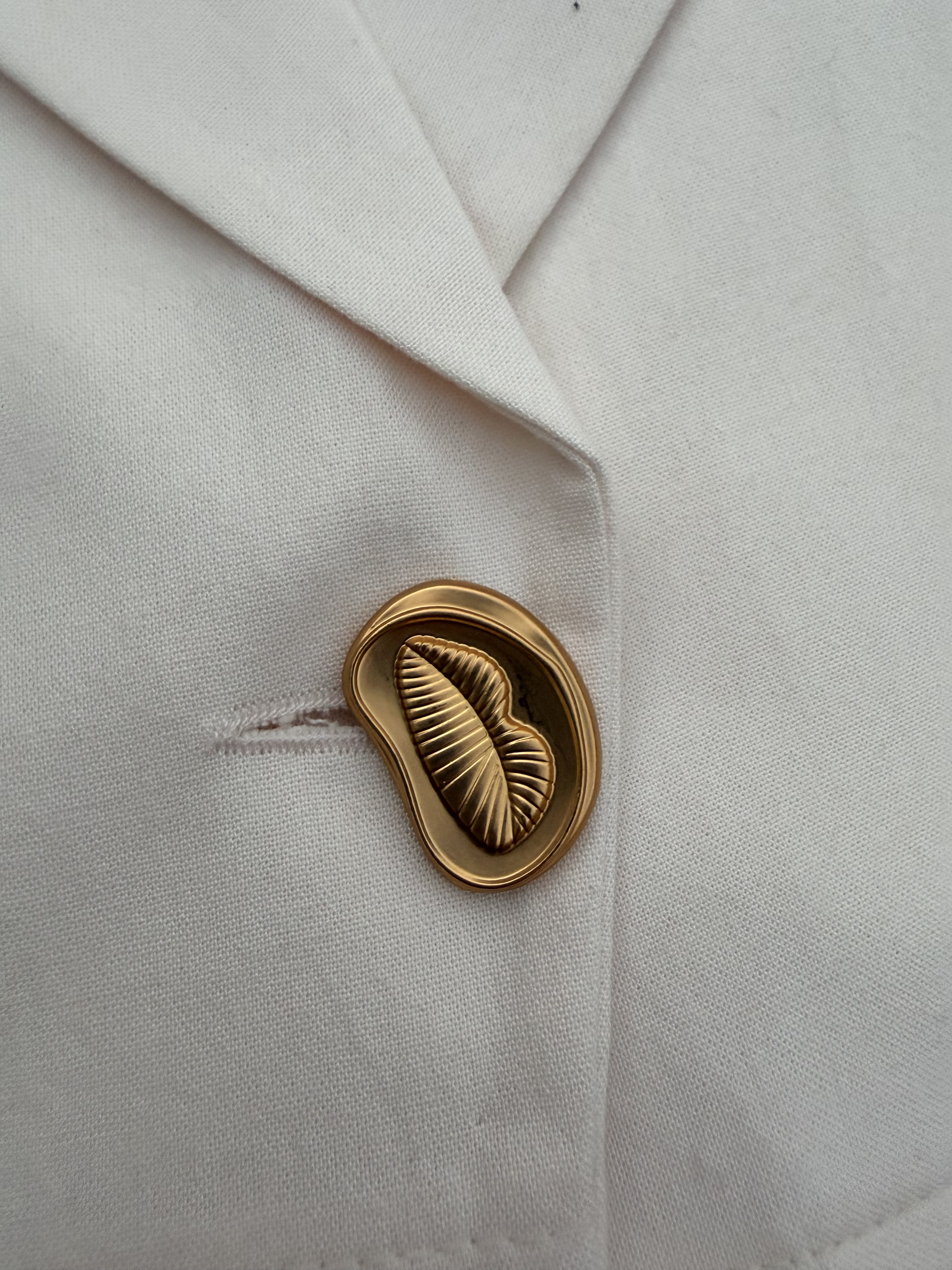 Close-up of gold-tone sculptural button on cream WIP tailored vest.