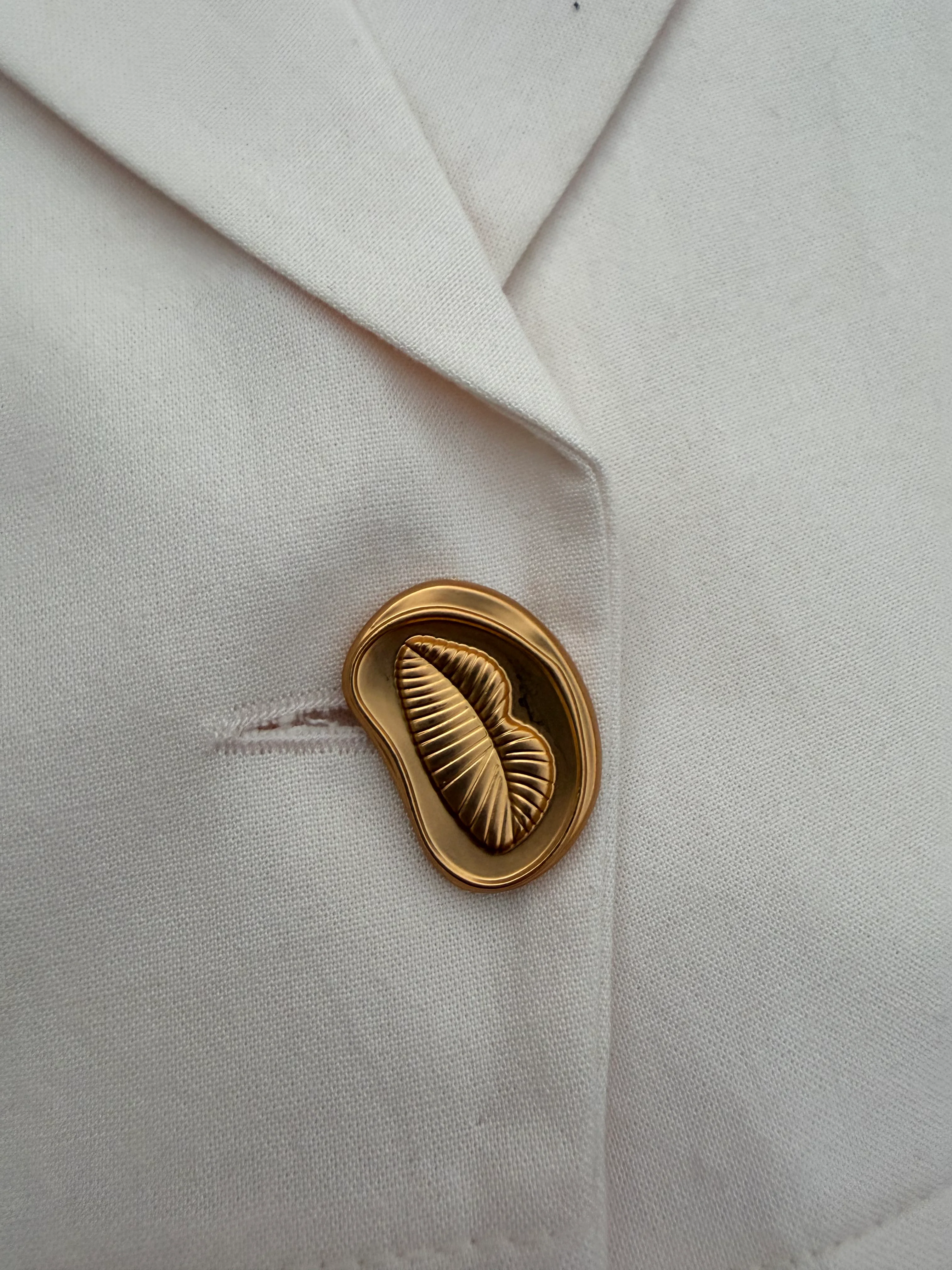 Close-up of gold-tone sculptural button on cream WIP tailored vest.