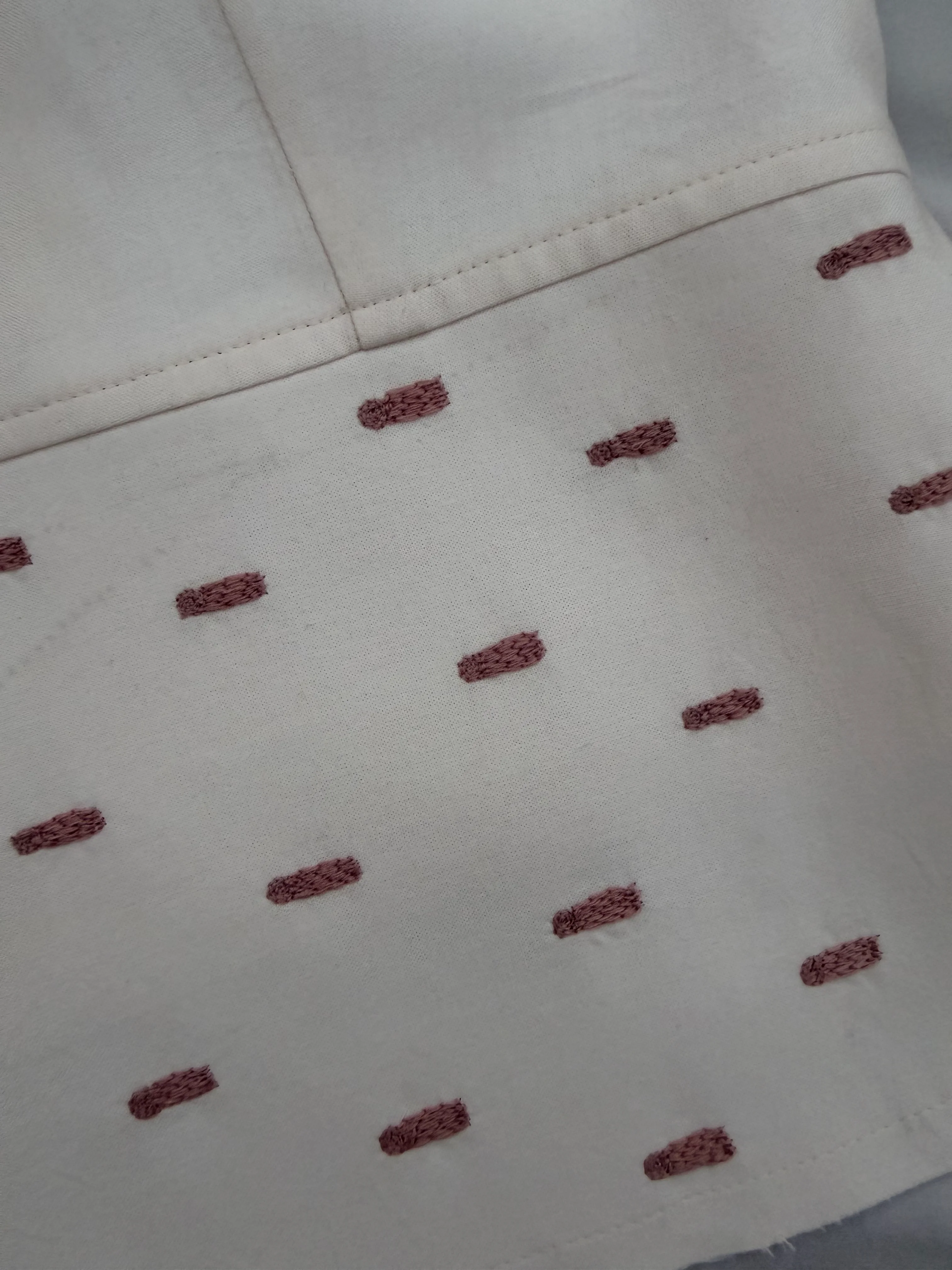 Close-up of mauve raised stitch motifs on cream WIP tailored vest.